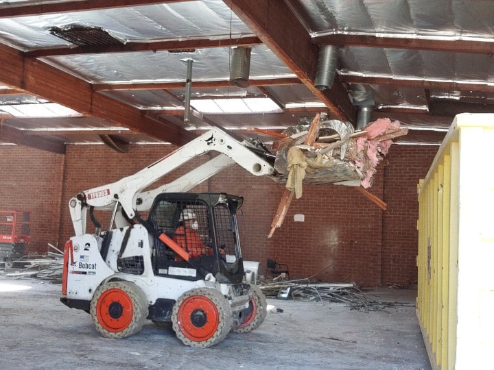 bobcat dumping demolition debris in dumpster