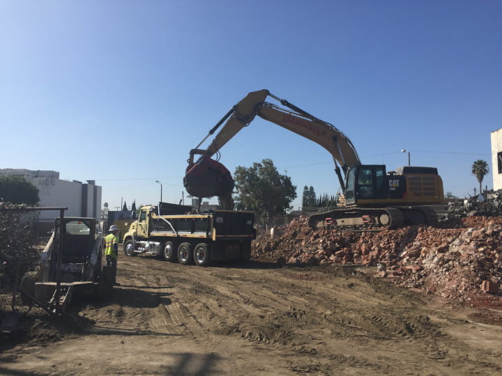 excavator unloading debris into dumpster bin with heavy-duty clamshell bucket