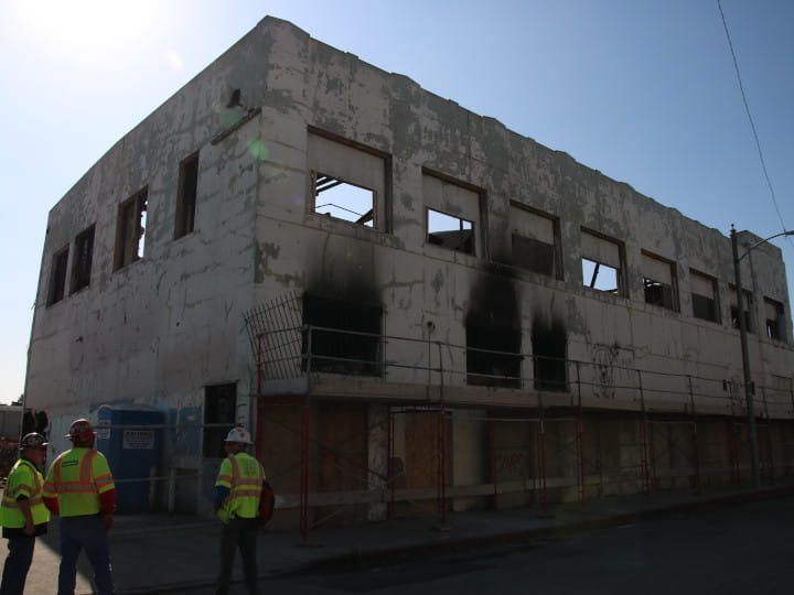 buildng wall about to be demolished by excatavor equipped with heavy-duty clamshell bucket
