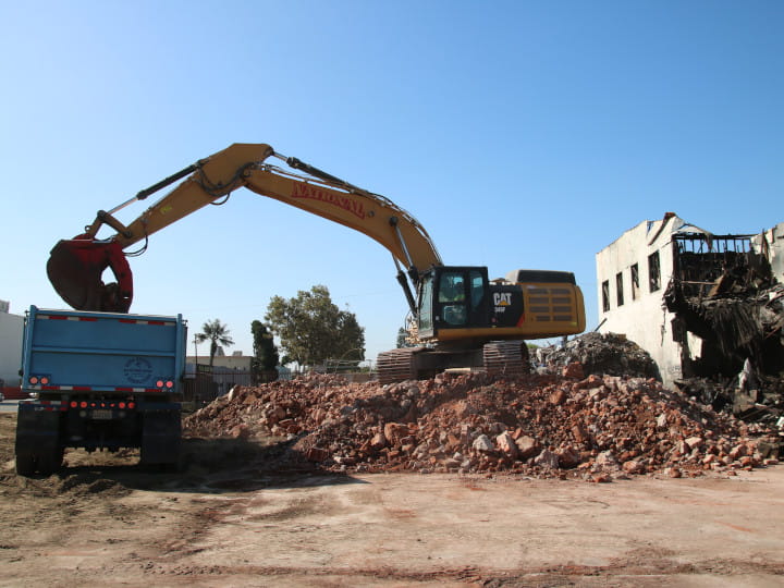 excavator unloading debris into dumpster bin with heavy-duty clamshell bucket